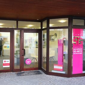 Eingang eines Telekom Shops mit 5G-Werbung und DPD-Paketservice im Schaufenster.