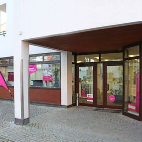 Telekom Shop mit 5G Werbung und pinker Flagge vor dem Eingang auf gepflastertem Weg.
